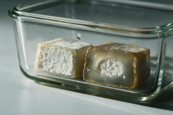 Zwei Stücke Graukäse in einer Glasdose im Vergleich: links ein junger mit krümeligem weißem Kern und schmalem Rand, rechts ein weiter gereifter mit breitem glasigem Rand und nur noch kleinem hellem Kern